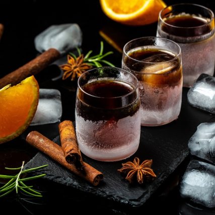 frozen herb liqueur in small glass. Shot glass of herb liqueur with cinnamon and oranges on a dark background.